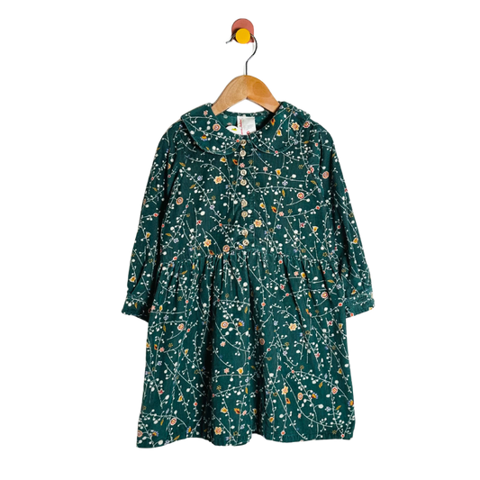 Green floral dress on a wooden hanger against a white background