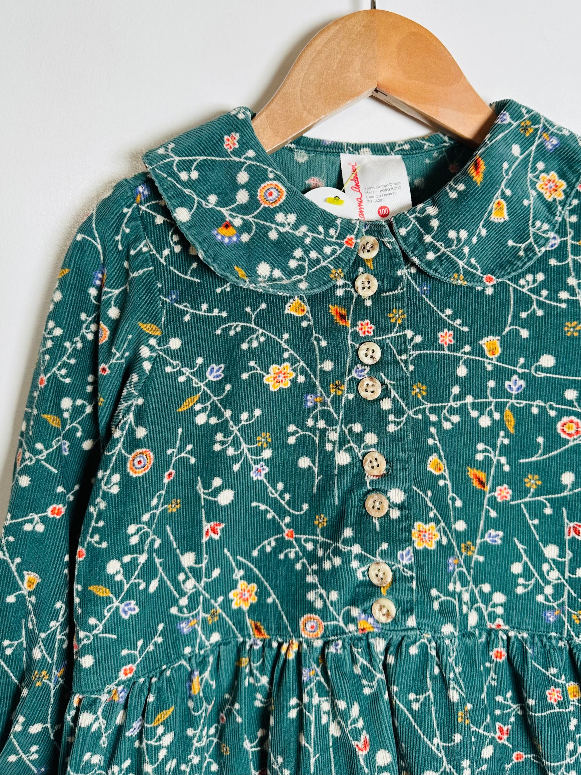 Green floral dress on a hanger against a white background