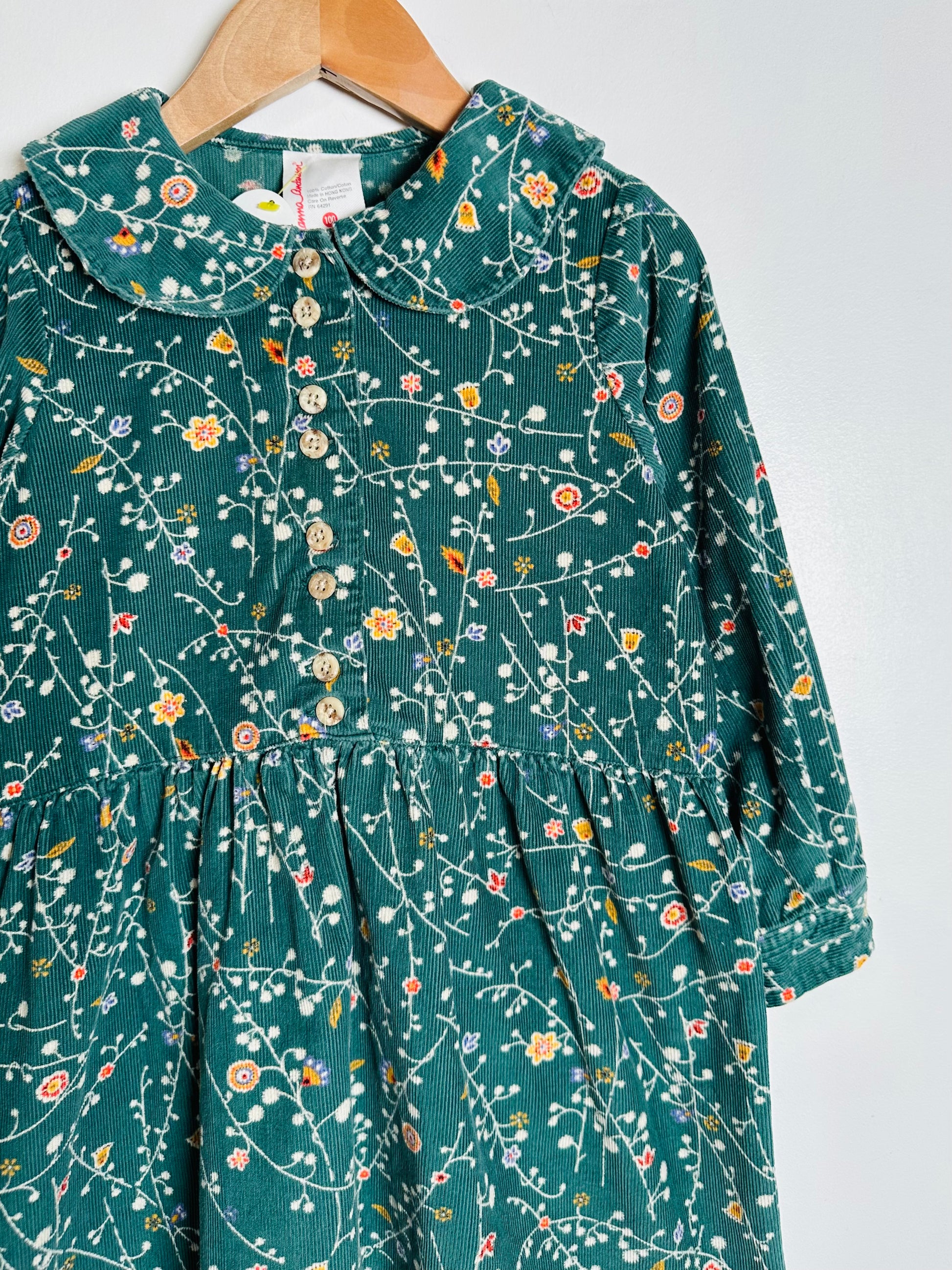 Green dress with floral pattern on a hanger against a white background