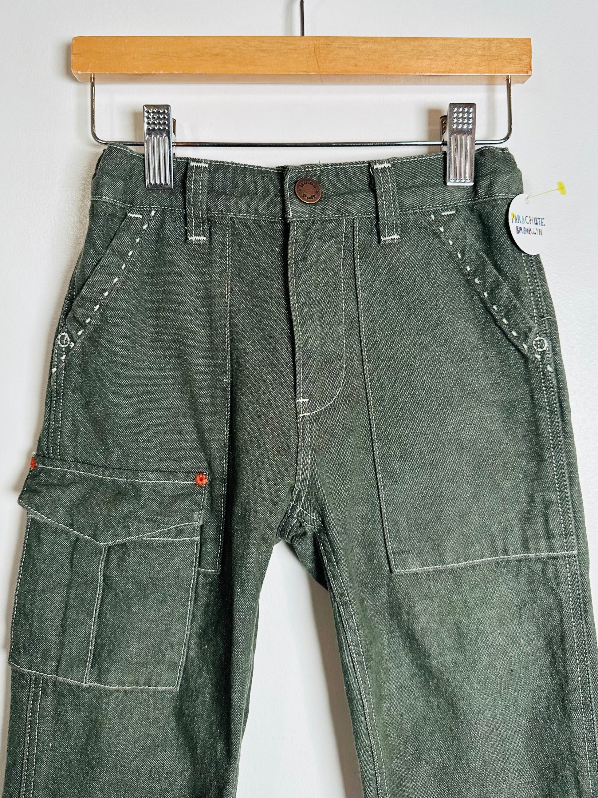 Green work pants with multiple pockets on a hanger against a white background