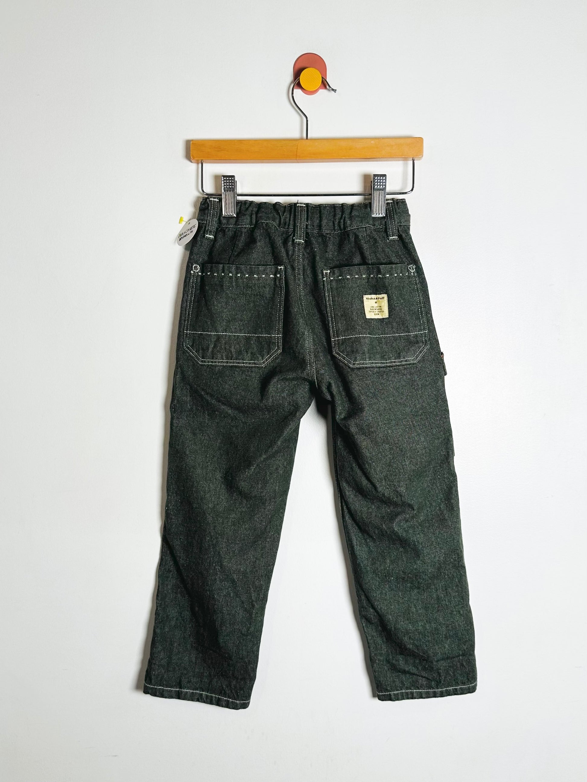 Dark green pants hanging on a wooden hanger against a white background