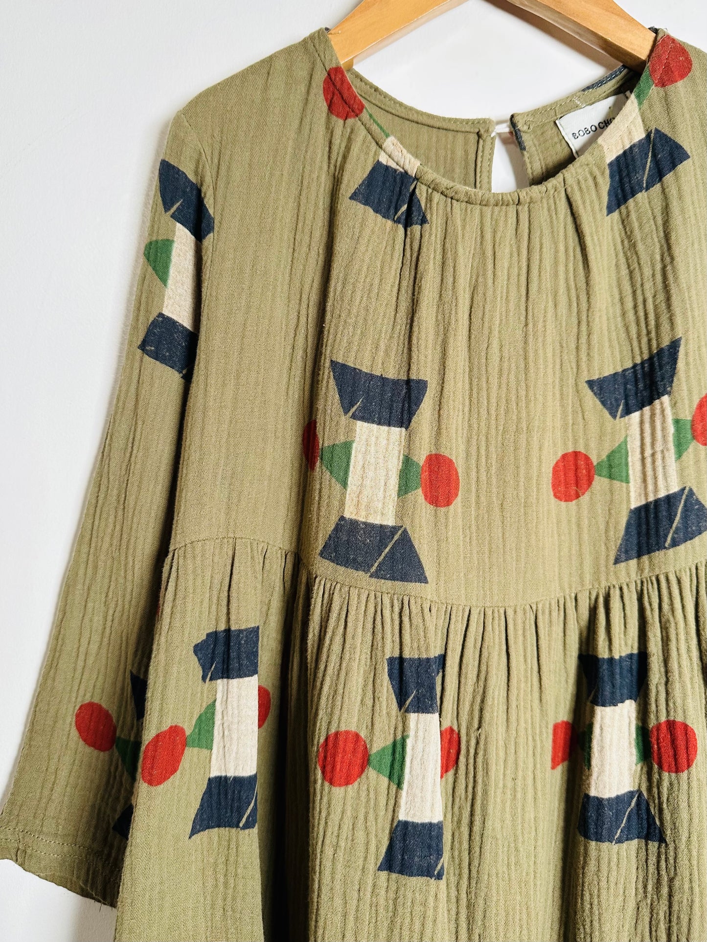 Green dress with geometric pattern on a hanger against a white background