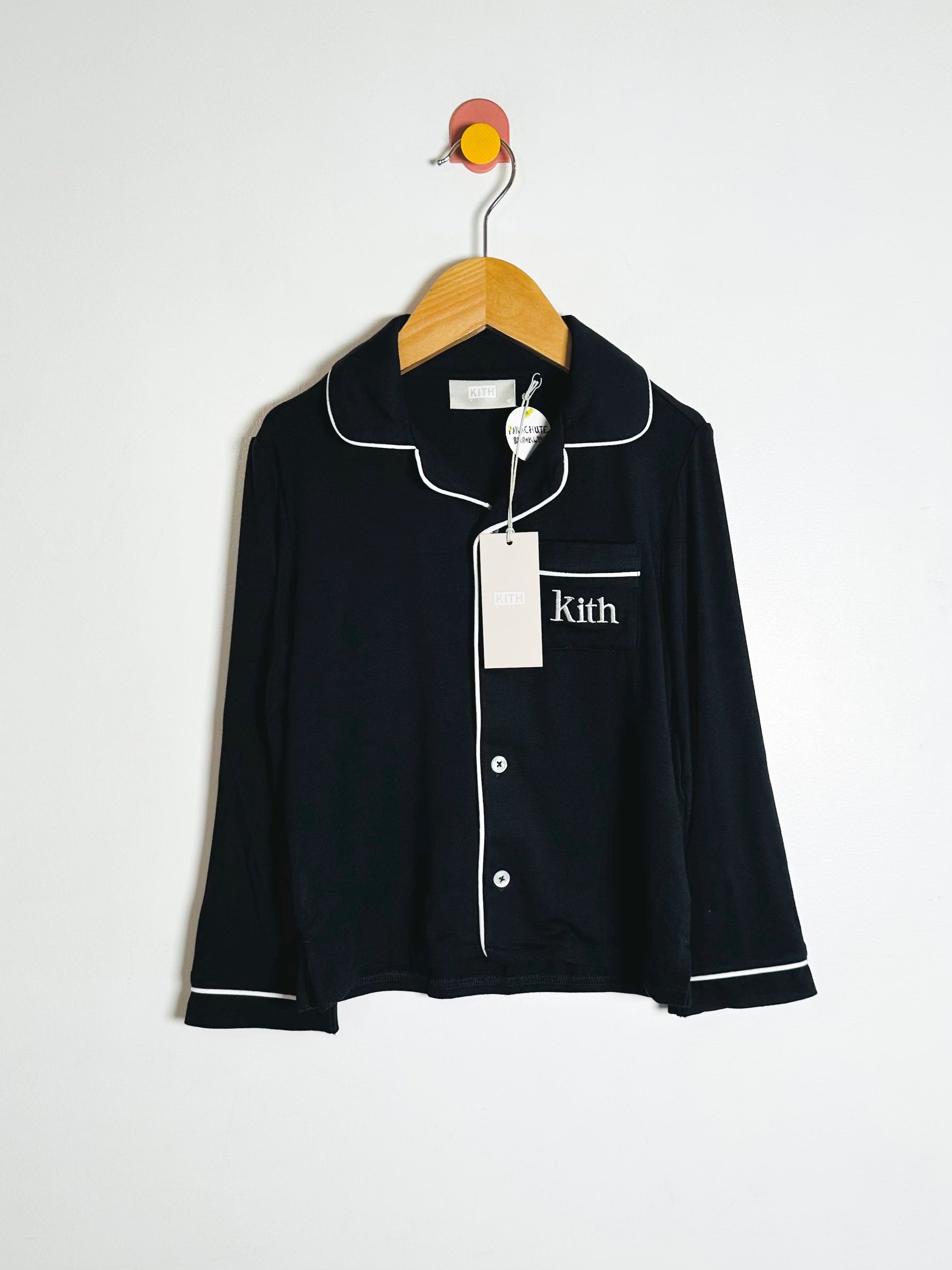 Black pajama top with white piping on a hanger against a white background