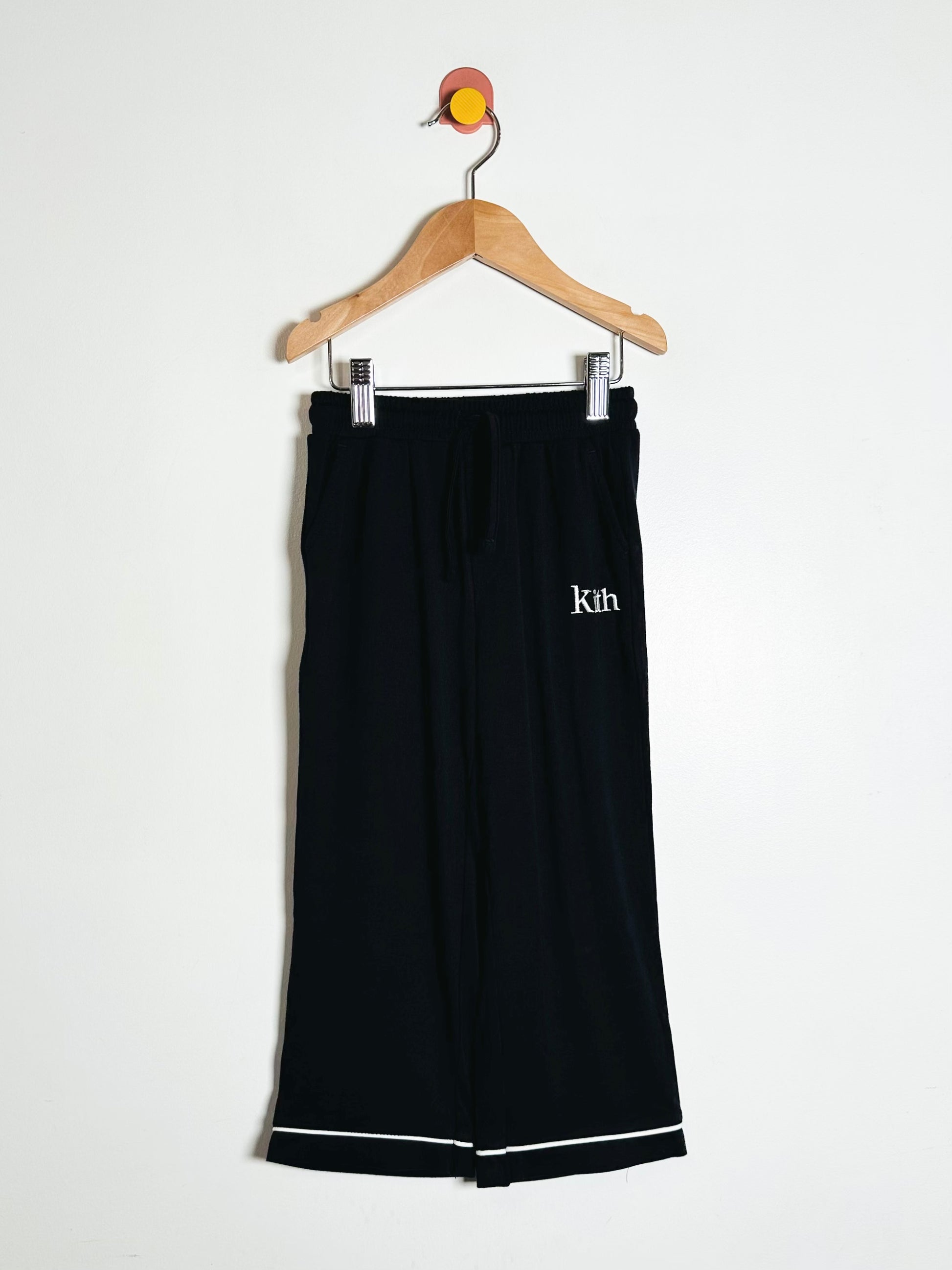 Black pants with 'Kith' logo on a hanger against a white background