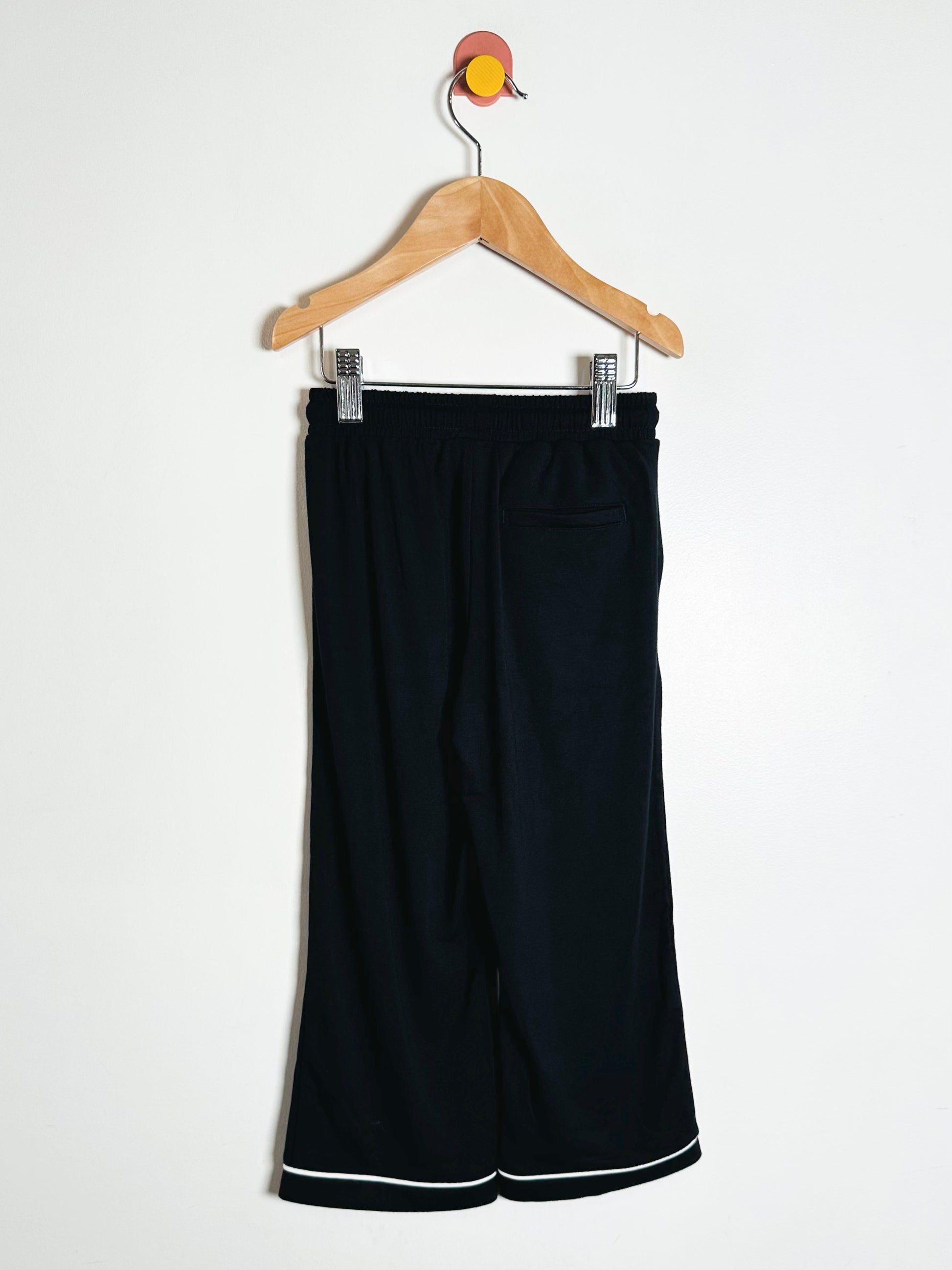 Black pants with white trim on a hanger against a white background