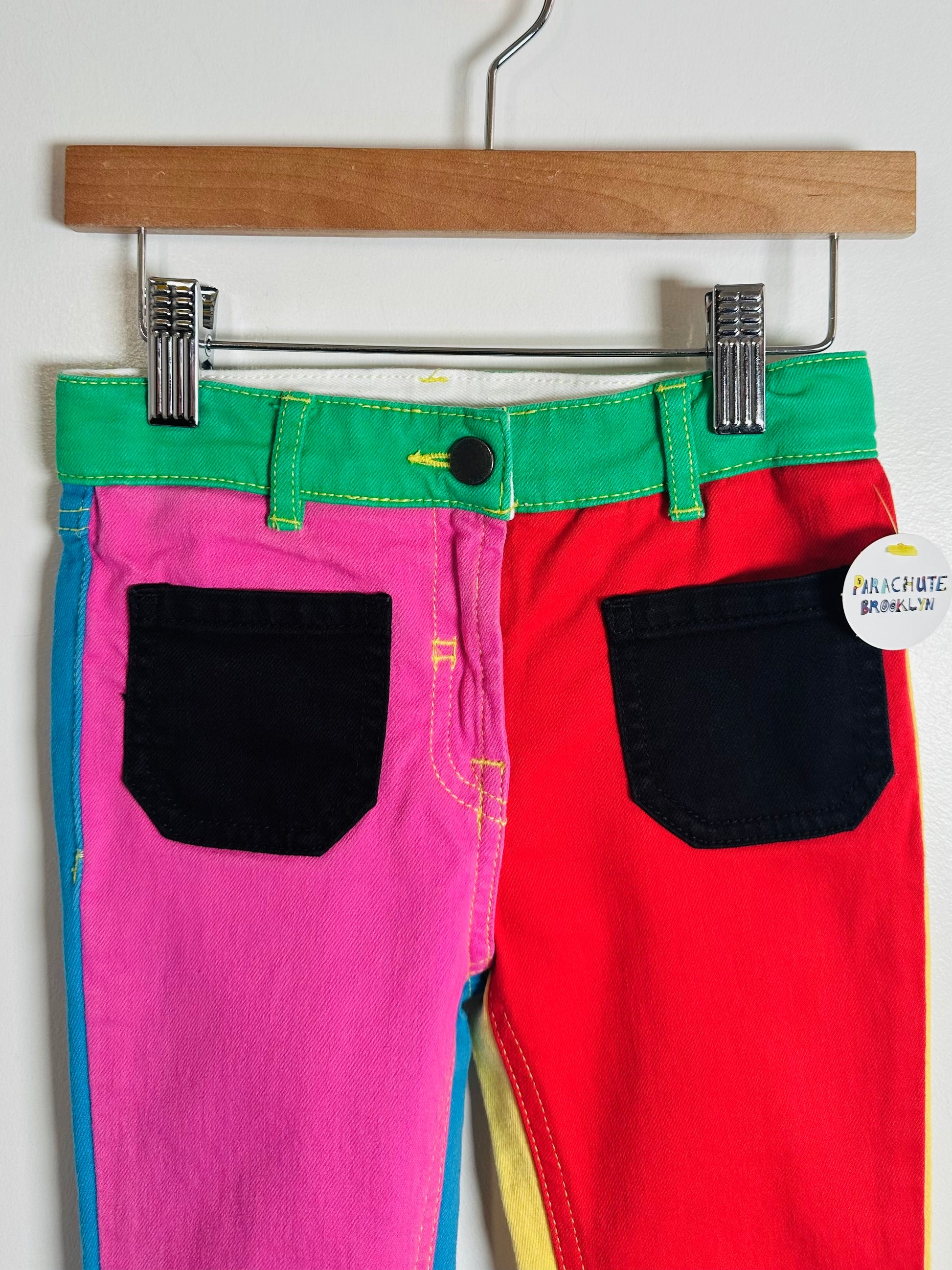 Colorful pants with green, pink, and red sections hanging on a wooden hanger.