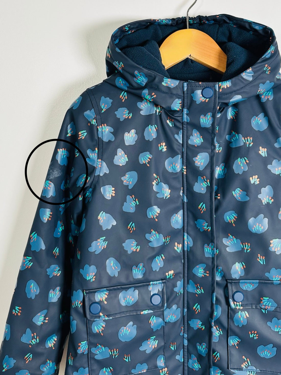 A hooded children's jacket in navy blue with a light blue and orange abstract floral pattern, hanging on a wooden hanger against a plain light background.