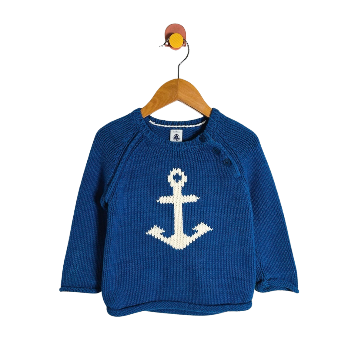 A blue knit baby sweater with a white knitted anchor on the front, hanging on a wooden hanger against a plain white background.
