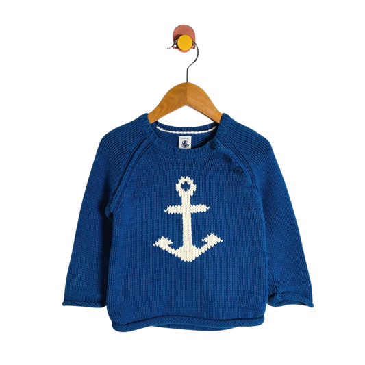 A blue knit baby sweater with a white knitted anchor on the front, hanging on a wooden hanger against a plain white background.