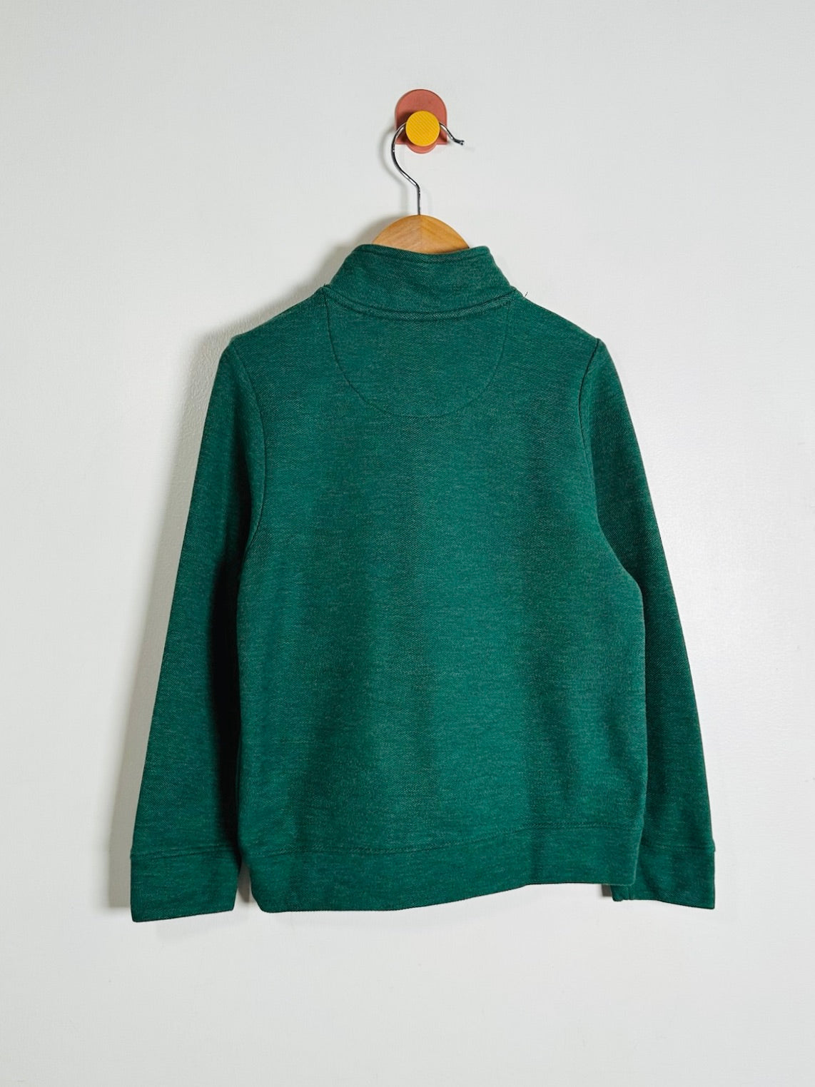 A dark green long-sleeve mock neck sweater hanging on a wooden hanger against a plain white wall.