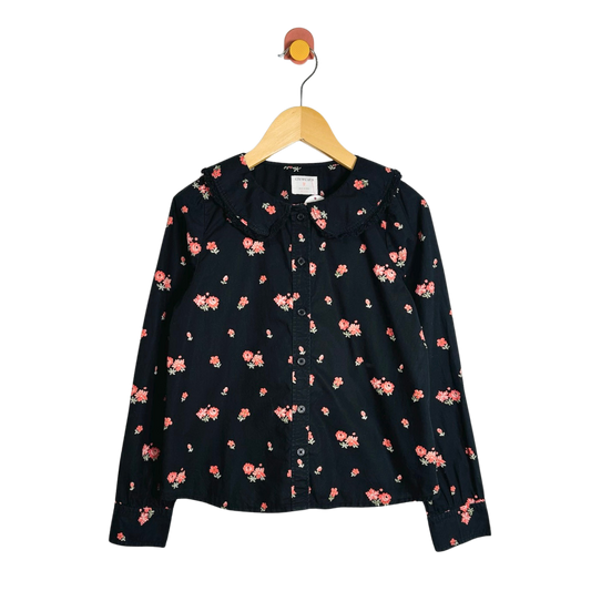 A black long-sleeve button-up blouse with a small pink and orange floral print, hanging on a wooden hanger against a white background.
