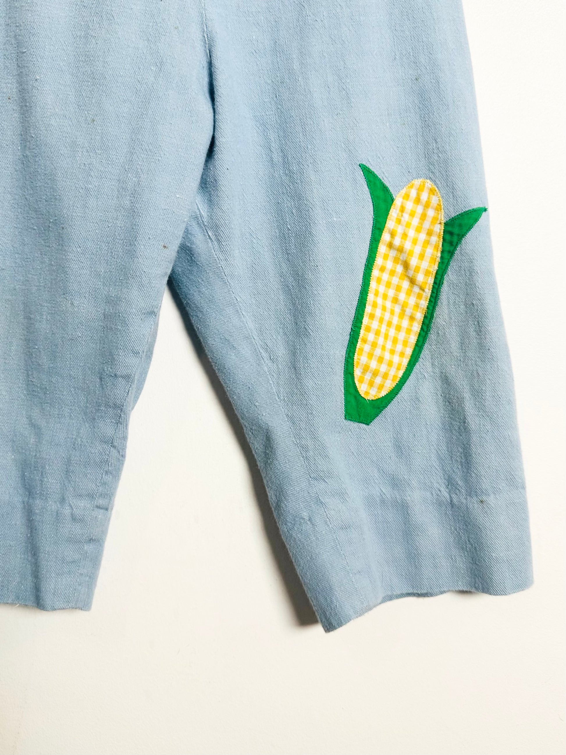 Blue overalls with a corn applique on a white background