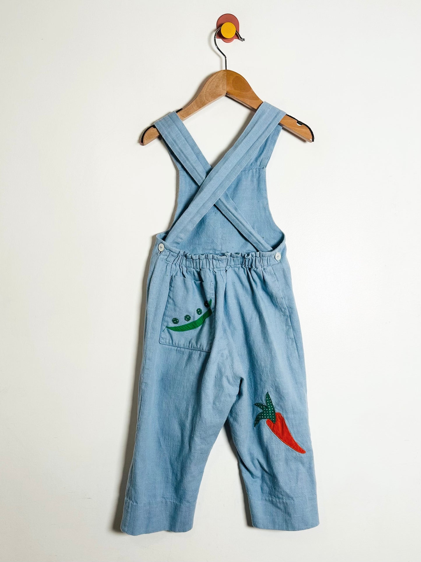 Blue denim overalls with embroidered designs on a white background