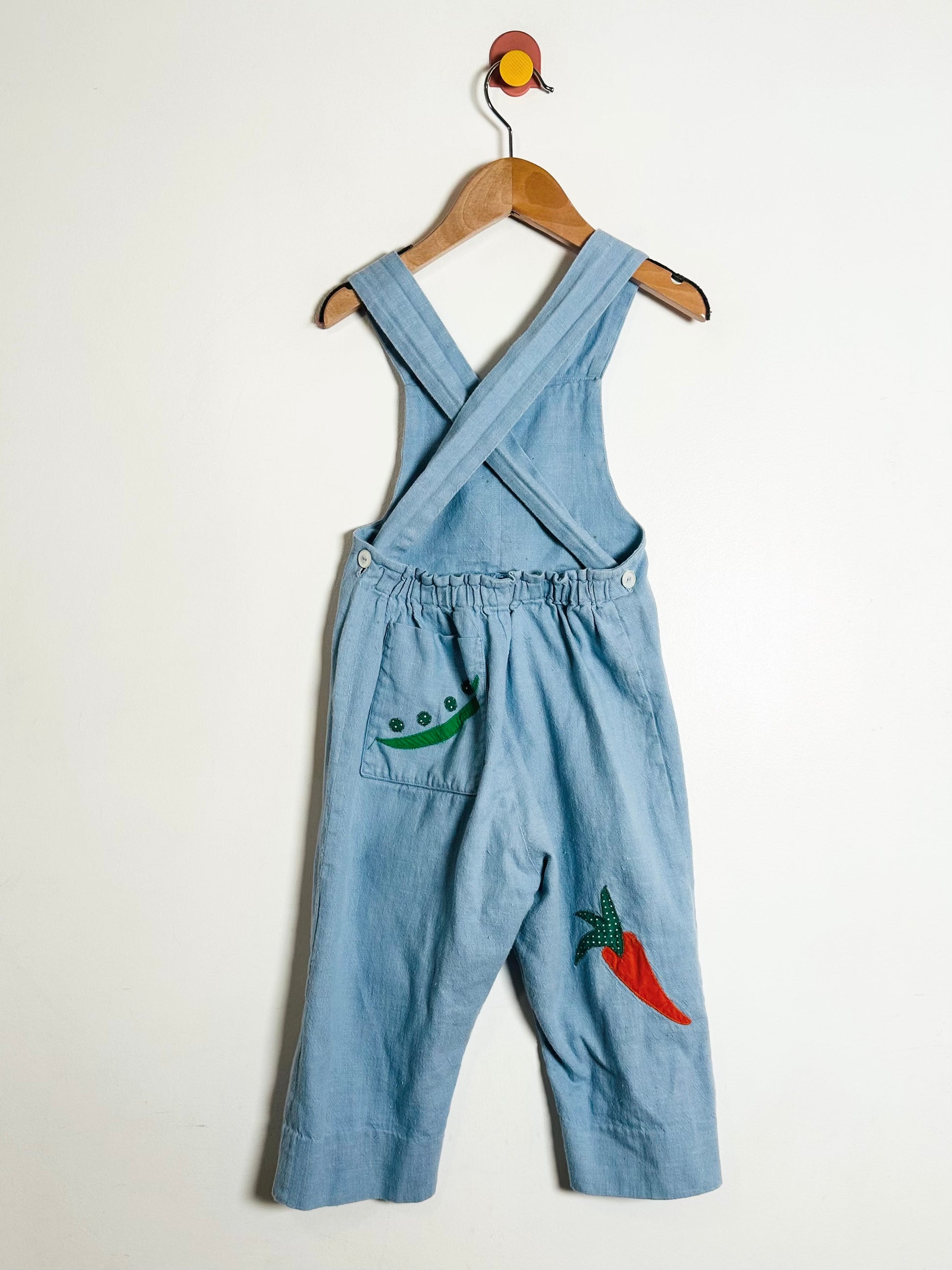 Blue denim overalls with embroidered designs on a white background