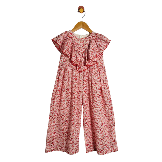 A children's floral jumpsuit with wide legs and ruffled cap sleeves, hanging on a wooden hanger against a plain white background.