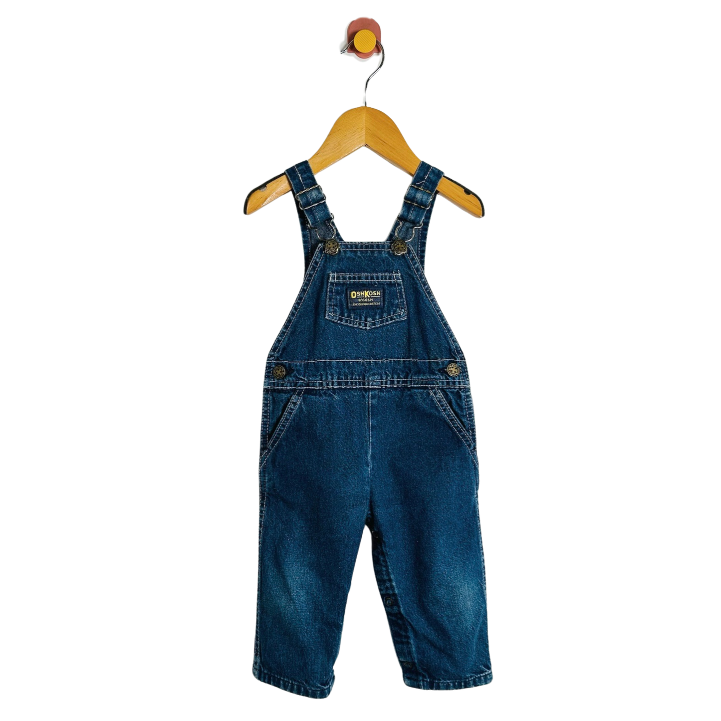 A pair of baby denim overall shorts in medium blue wash, hanging on a wooden hanger against a plain white background.