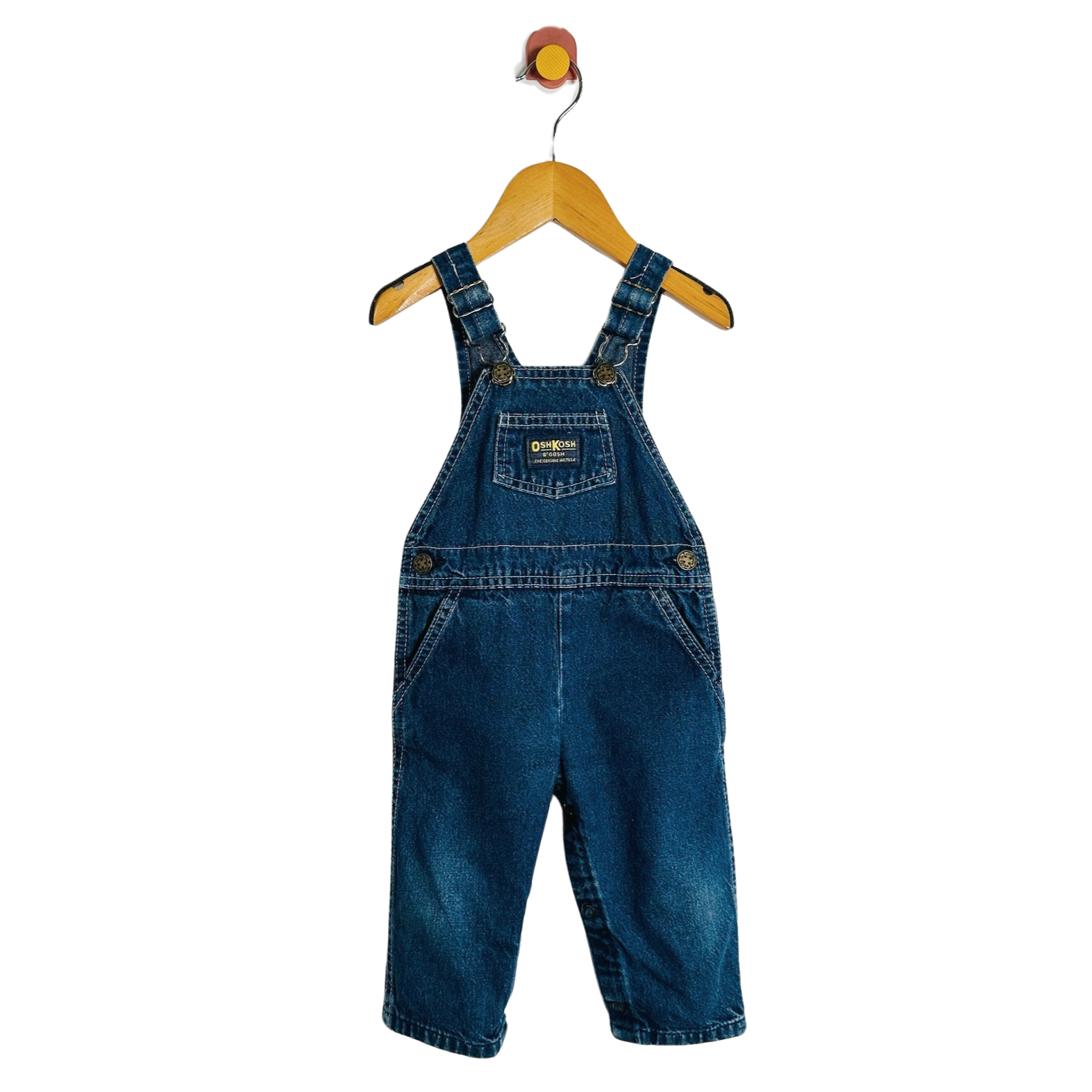 A pair of baby denim overall shorts in medium blue wash, hanging on a wooden hanger against a plain white background.
