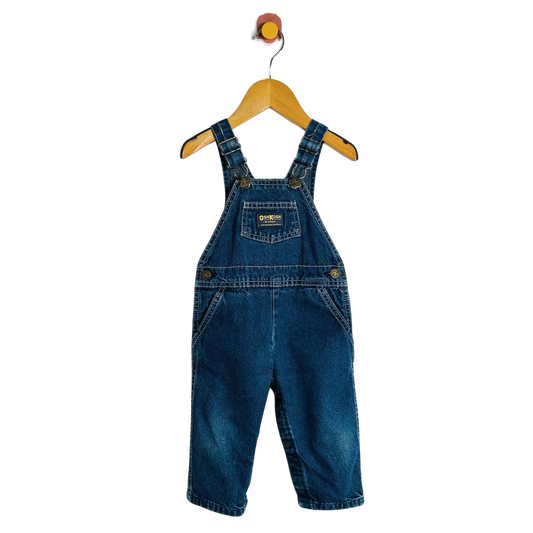 A pair of baby denim overall shorts in medium blue wash, hanging on a wooden hanger against a plain white background.