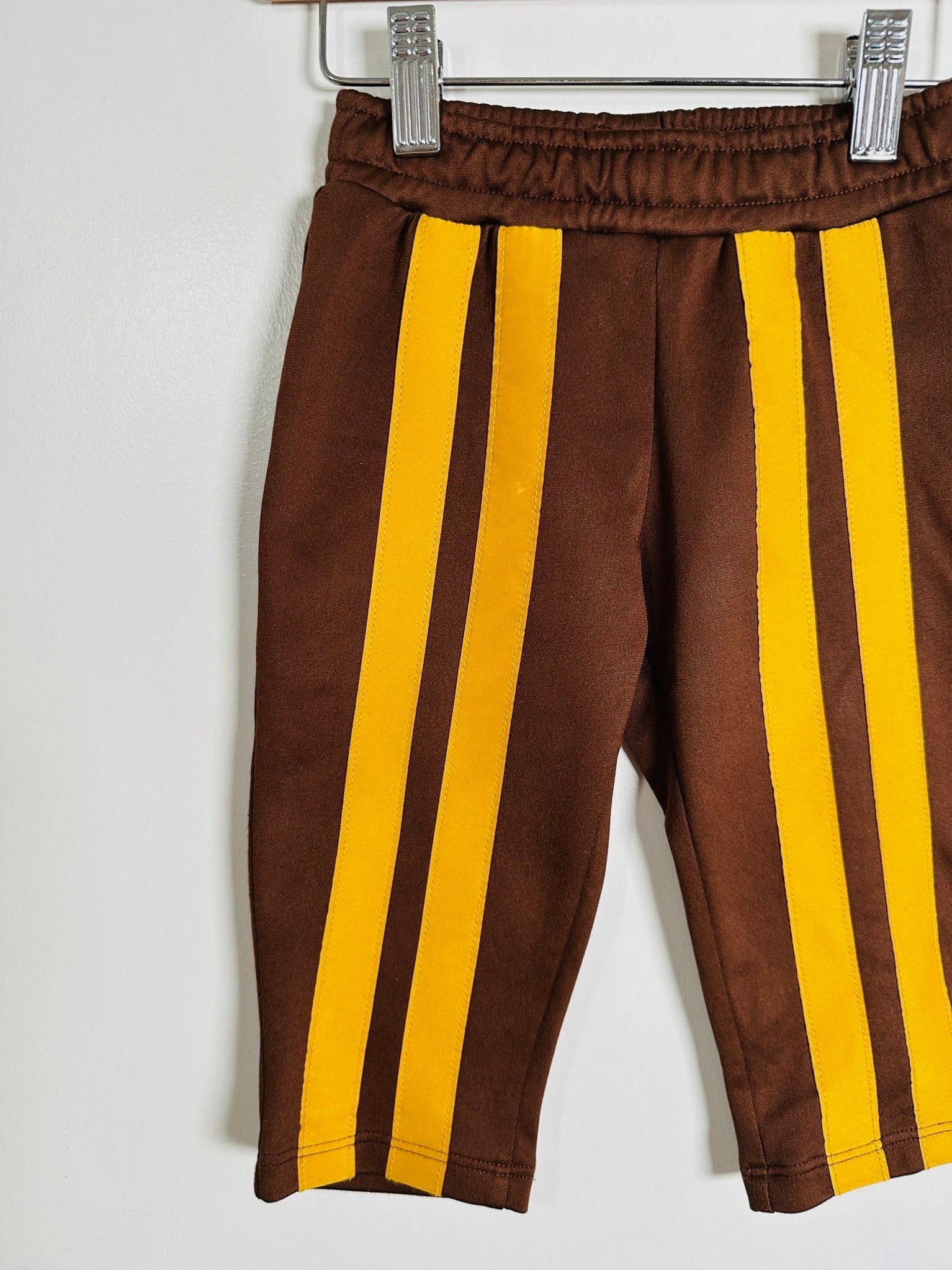 A pair of brown pants with bold yellow vertical stripes, hanging from a metal hanger against a plain white wall.