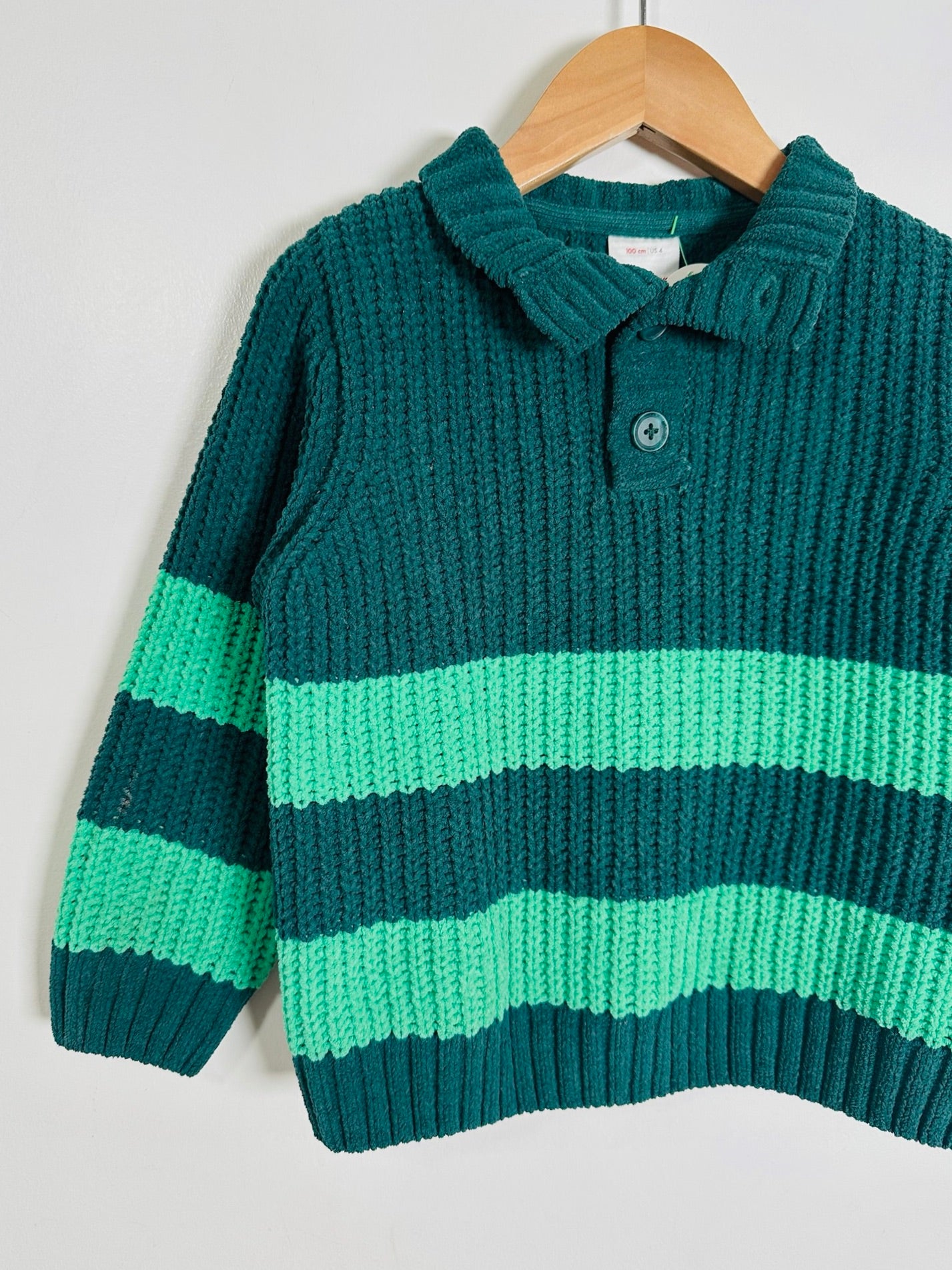 A dark teal green ribbed knit polo sweater with horizontal mint green stripes, hanging on a wooden hanger against a light gray background.