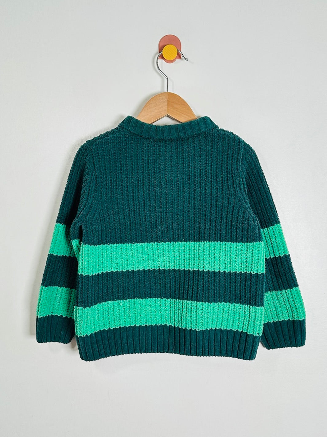 A dark green ribbed knit sweater with horizontal mint green stripes, hanging on a wooden hanger against a light gray wall.