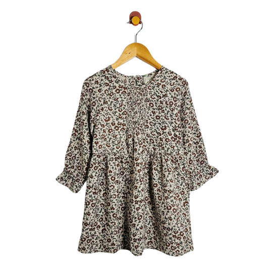 A long-sleeve babydoll dress with a brown and beige floral print pattern, hanging on a wooden hanger against a plain white background.