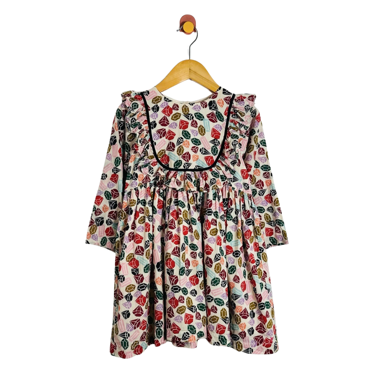 A long-sleeve baby dress with a colorful gemstone pattern, hanging on a wooden hanger against a plain white background.