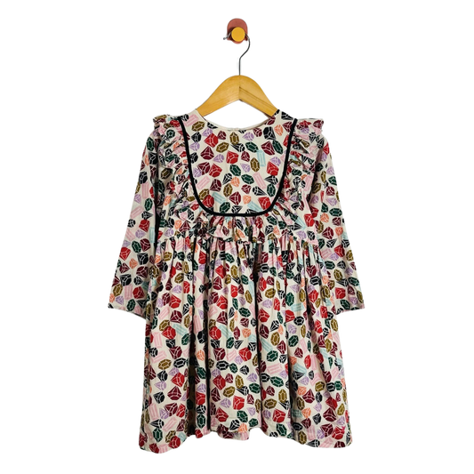 A long-sleeve baby dress with a colorful gemstone pattern, hanging on a wooden hanger against a plain white background.