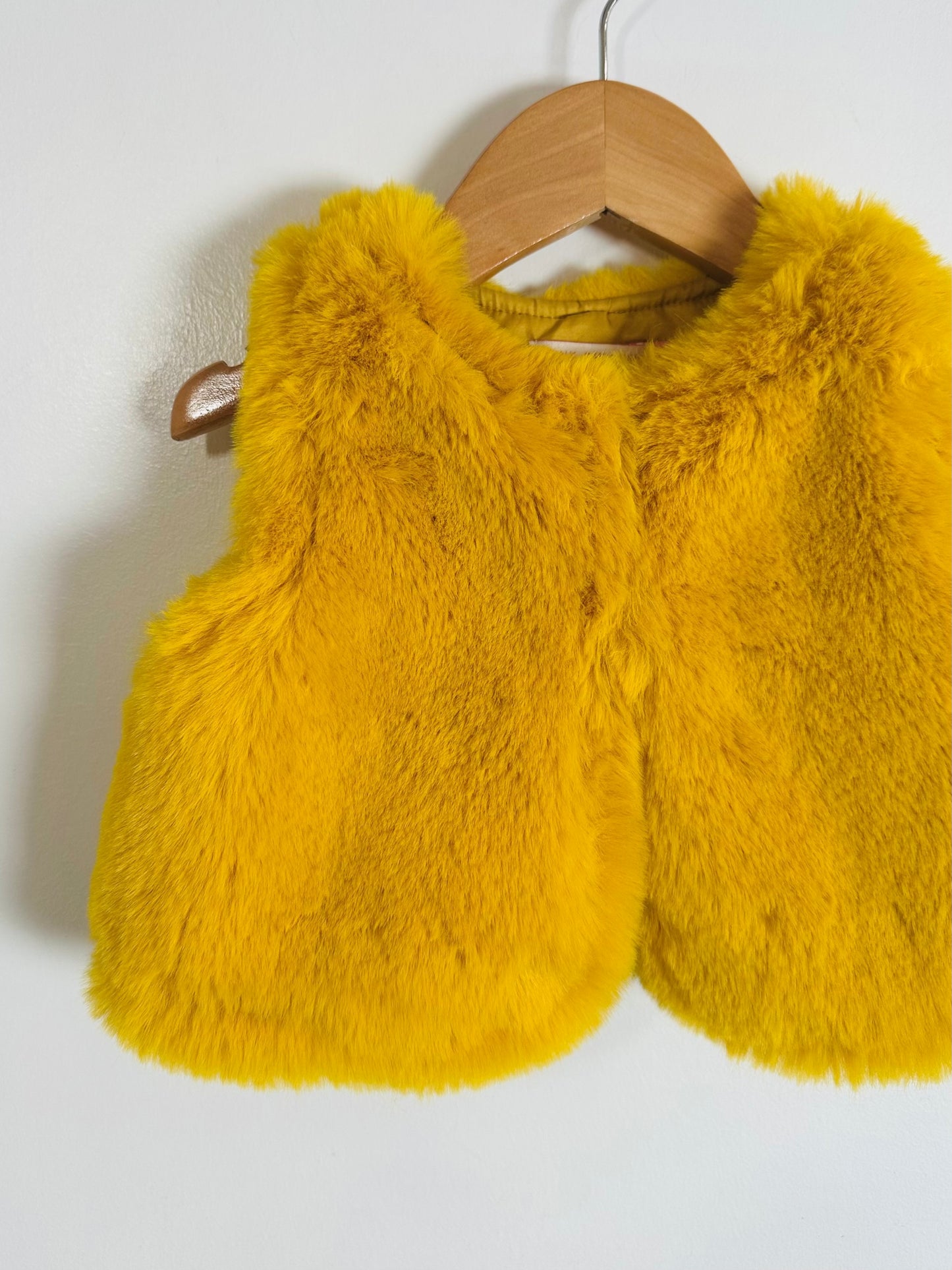 Yellow fluffy vest on a wooden hanger against a white background