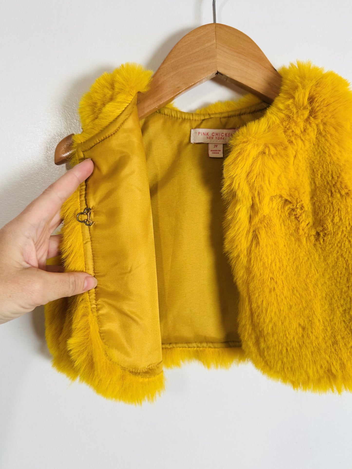 Yellow fur vest on a wooden hanger against a white background