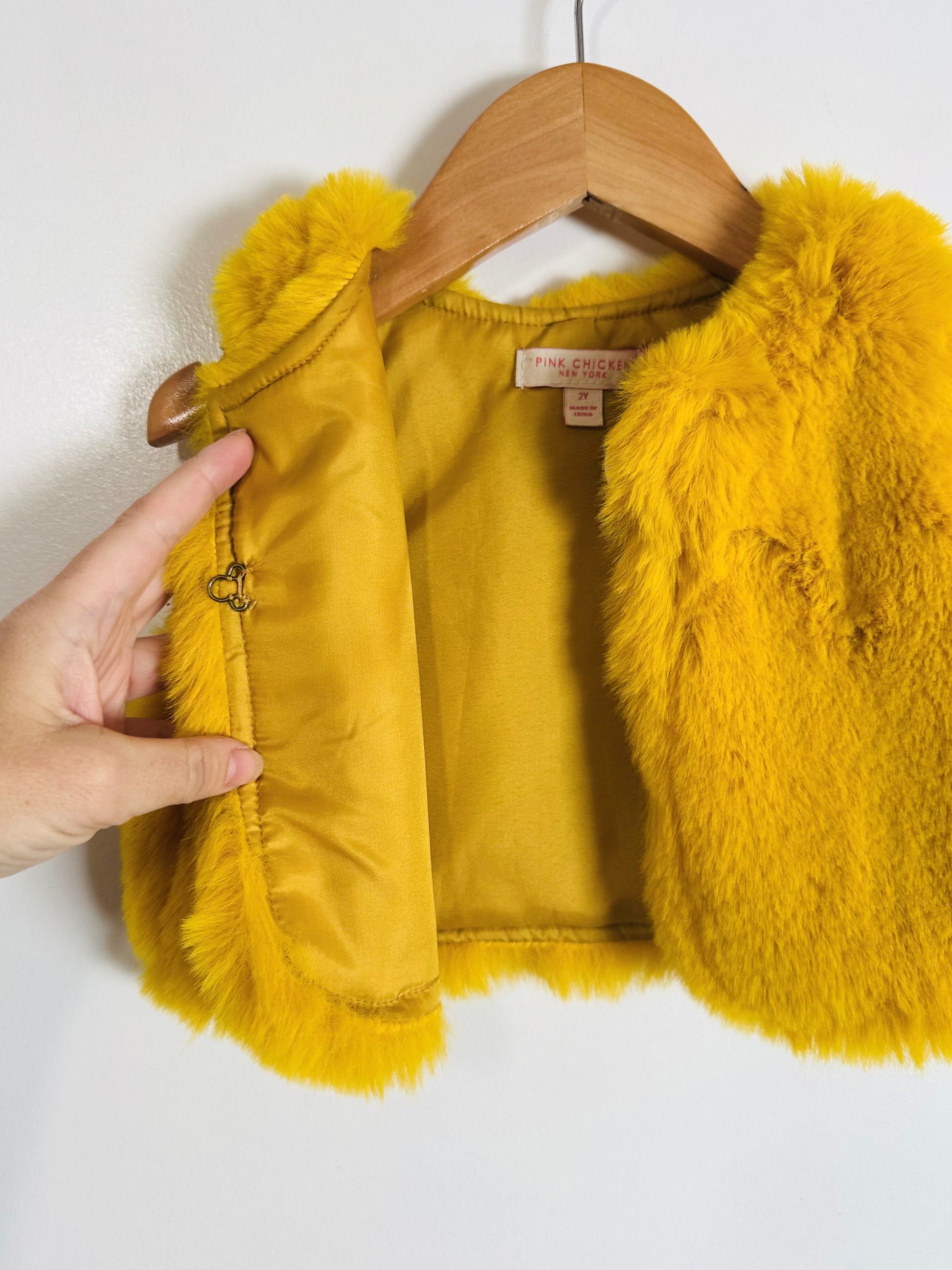 Yellow fur vest on a wooden hanger against a white background