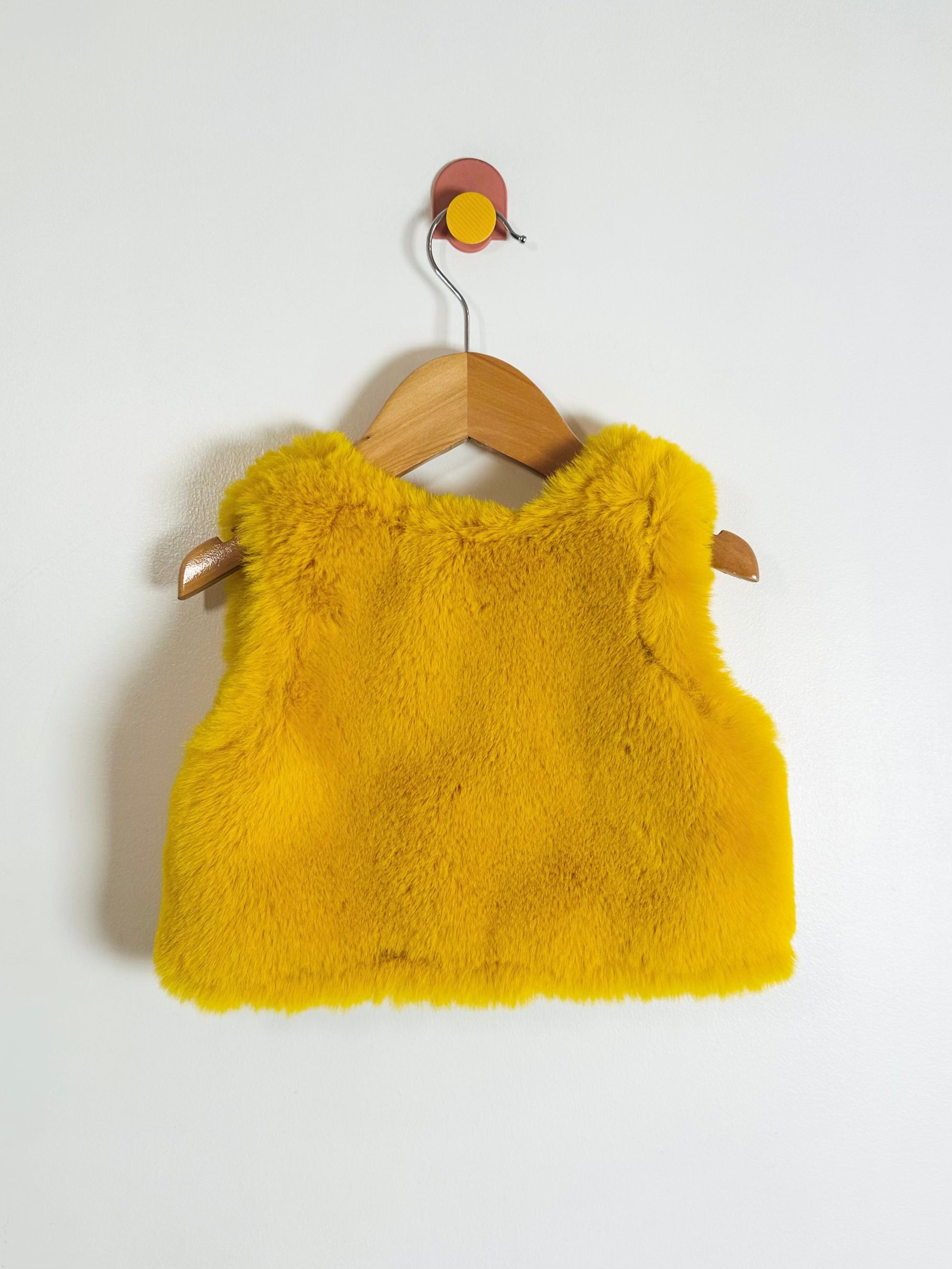 Yellow fluffy vest on a wooden hanger against a white background