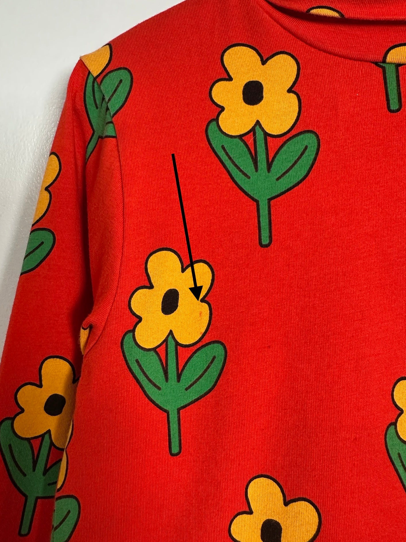 A close-up of a red sweatshirt featuring a repeating pattern of yellow flowers with green stems and leaves.