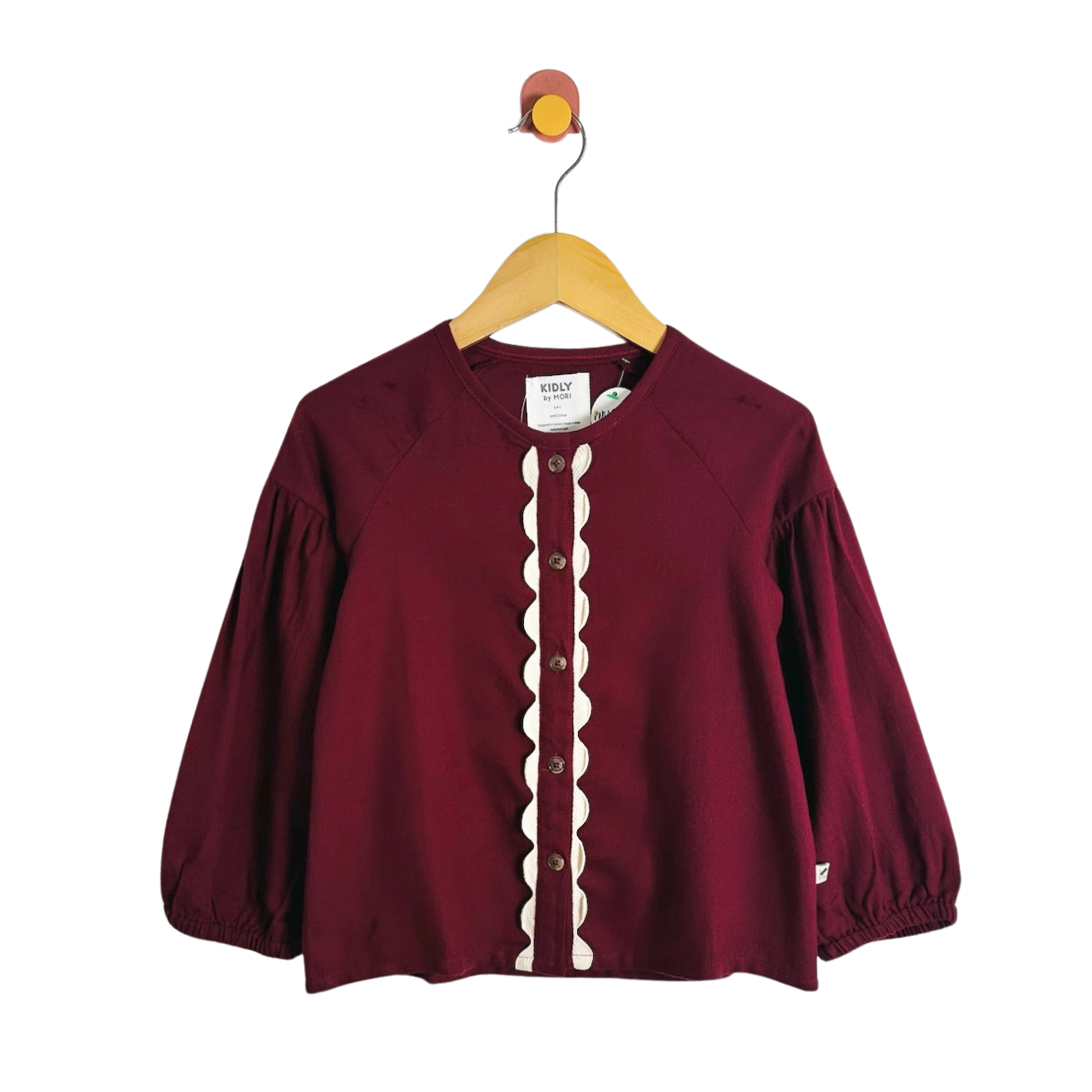 A burgundy long-sleeve raglan top with a cream scalloped placket and button front, hanging on a wooden hanger against a white background.