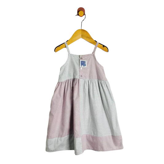 A baby girl's sleeveless dress with a dusty pink and white gingham patchwork design, hanging on a wooden hanger against a white background.