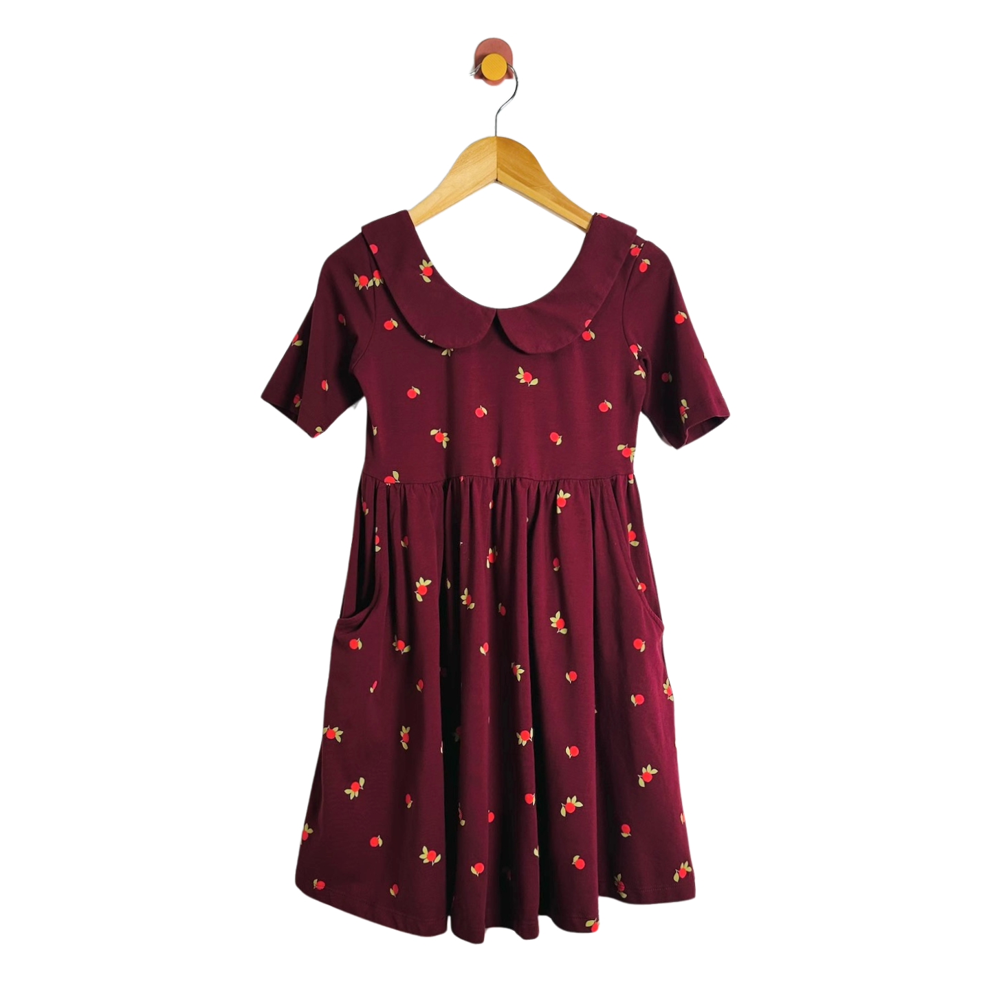 A short-sleeve babydoll dress in deep burgundy with a small red and yellow floral print, featuring a Peter Pan collar and side pockets, hanging on a wooden hanger against a plain white background.