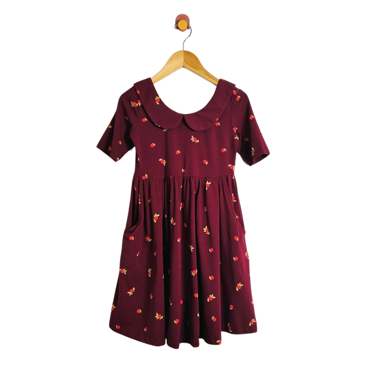 A short-sleeve babydoll dress in deep burgundy with a small red and yellow floral print, featuring a Peter Pan collar and side pockets, hanging on a wooden hanger against a plain white background.