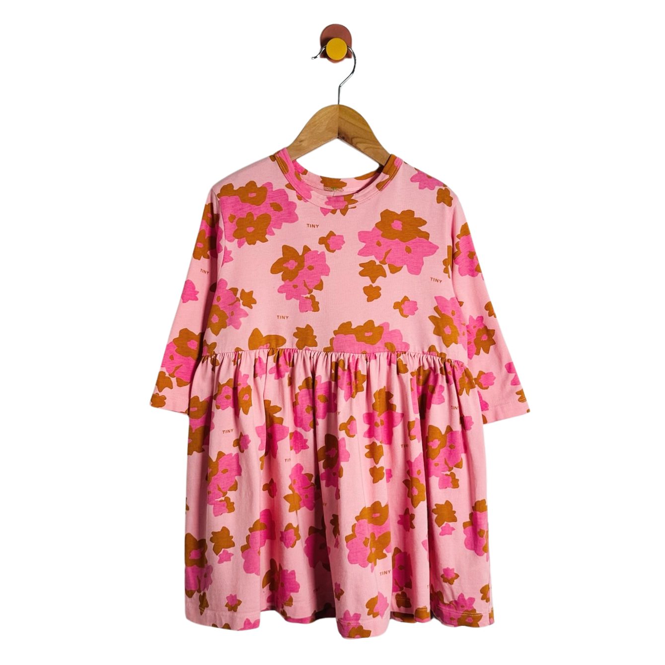 A pink long-sleeve dress with a bold orange and magenta floral pattern, hanging on a wooden hanger against a plain white background.