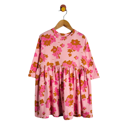 A pink long-sleeve dress with a bold orange and magenta floral pattern, hanging on a wooden hanger against a plain white background.