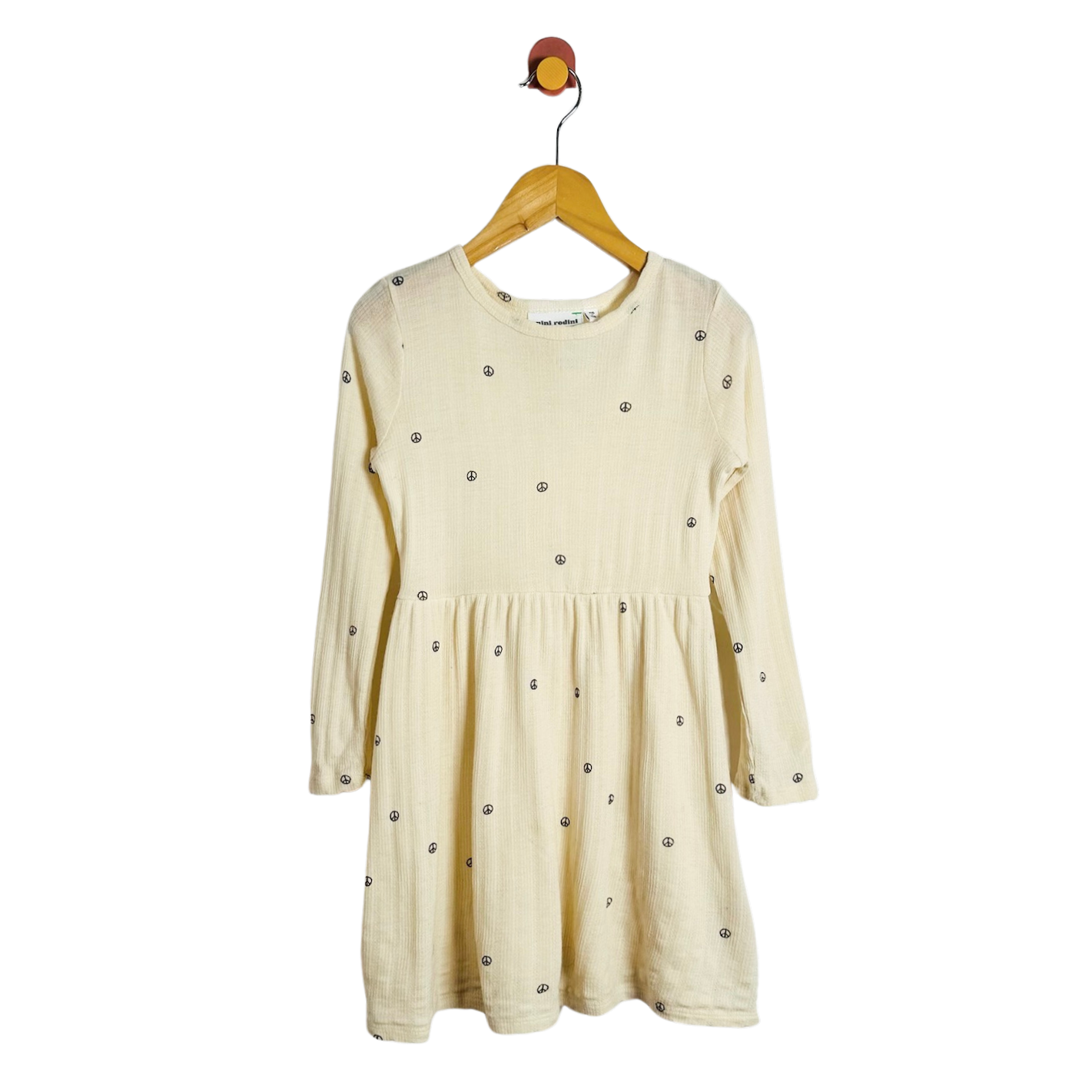 A cream-colored long-sleeve baby dress hanging on a wooden hanger against a plain white background.