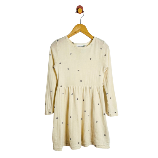 A cream-colored long-sleeve baby dress hanging on a wooden hanger against a plain white background.