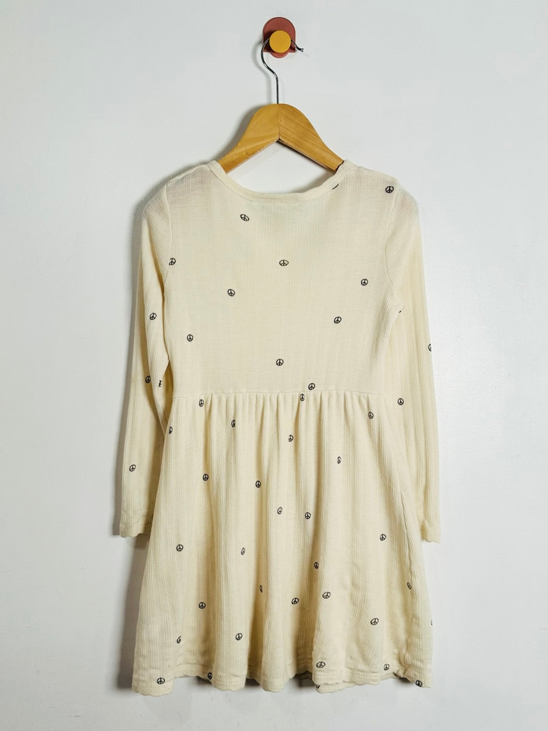 A cream-colored long-sleeve dress with small metallic silver dots, hanging on a wooden hanger against a plain white wall.