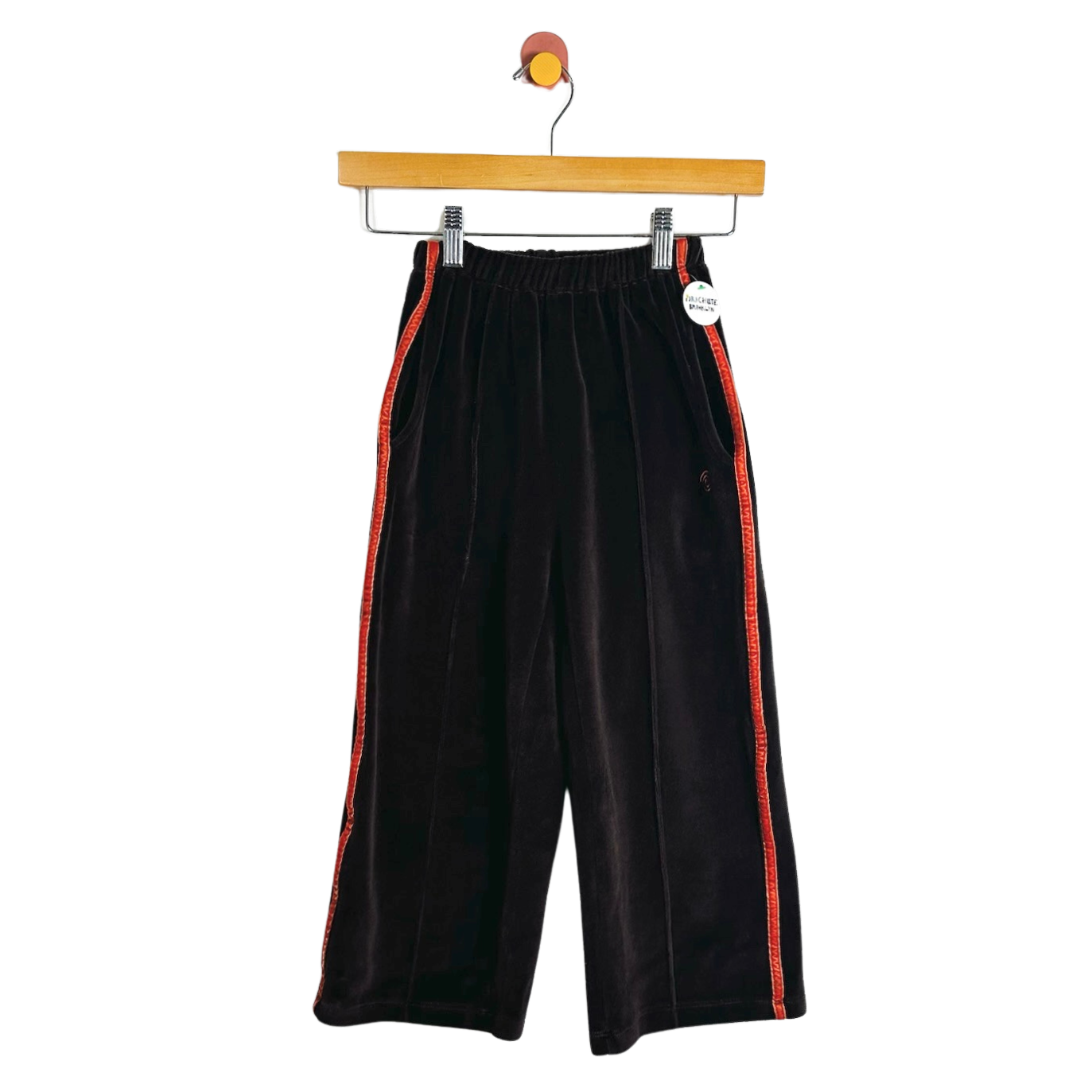 Black wide-leg cropped pants with red side stripes, hanging on a wooden hanger against a white background.