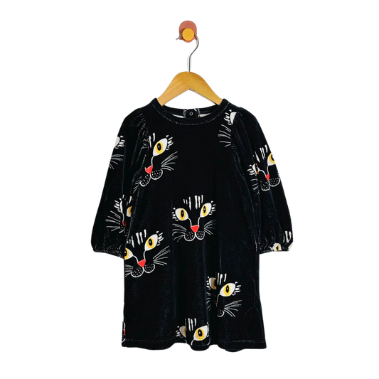 A black velvet long-sleeve dress with an all-over cartoon cat face print, hanging on a wooden hanger against a plain white background.