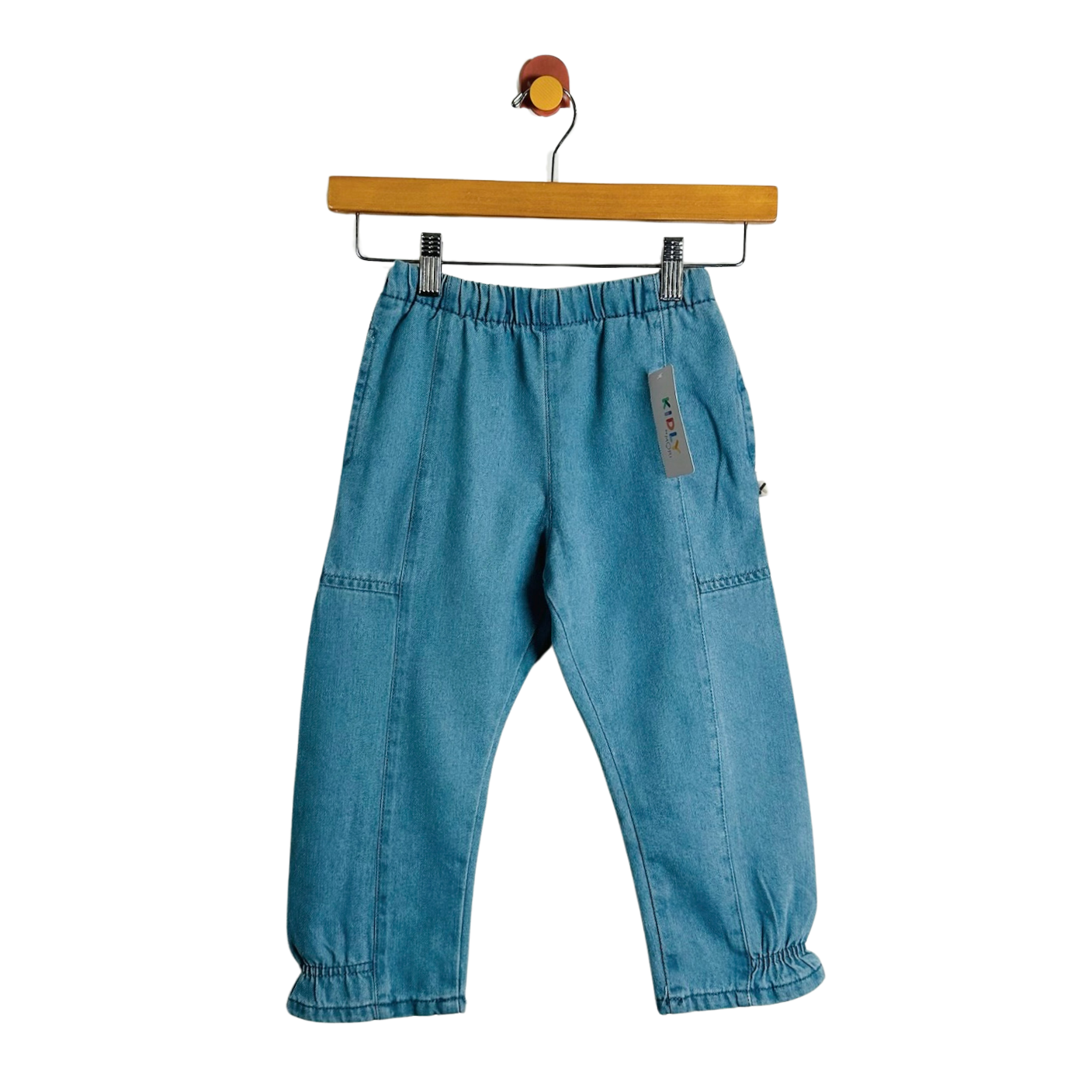 A pair of blue denim pants with an elastic waistband and gathered ankle cuffs, hanging from a wooden hanger against a plain white background.
