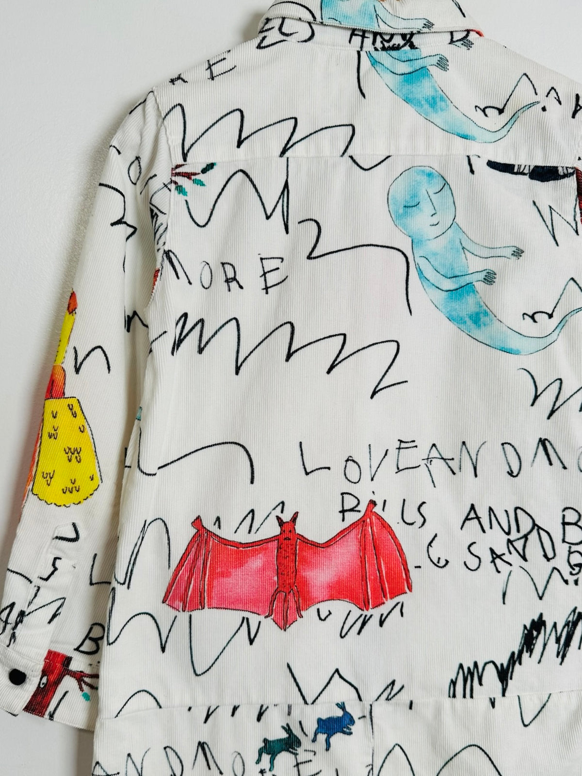 A close-up of a white shirt featuring a whimsical, hand-drawn doodle print with black scribbles, blue cartoon figures, a red bird, and yellow accents.