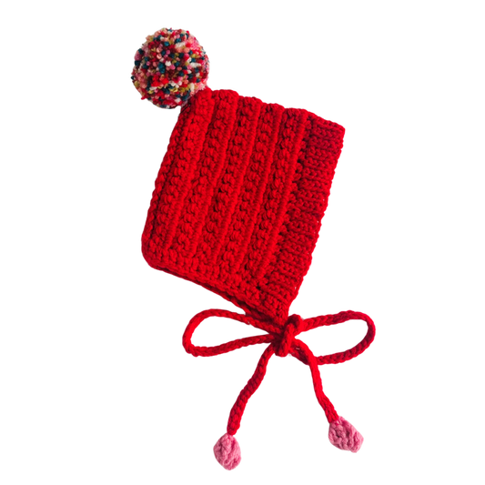 Red knitted baby hat with colorful pom-pom on a white background
