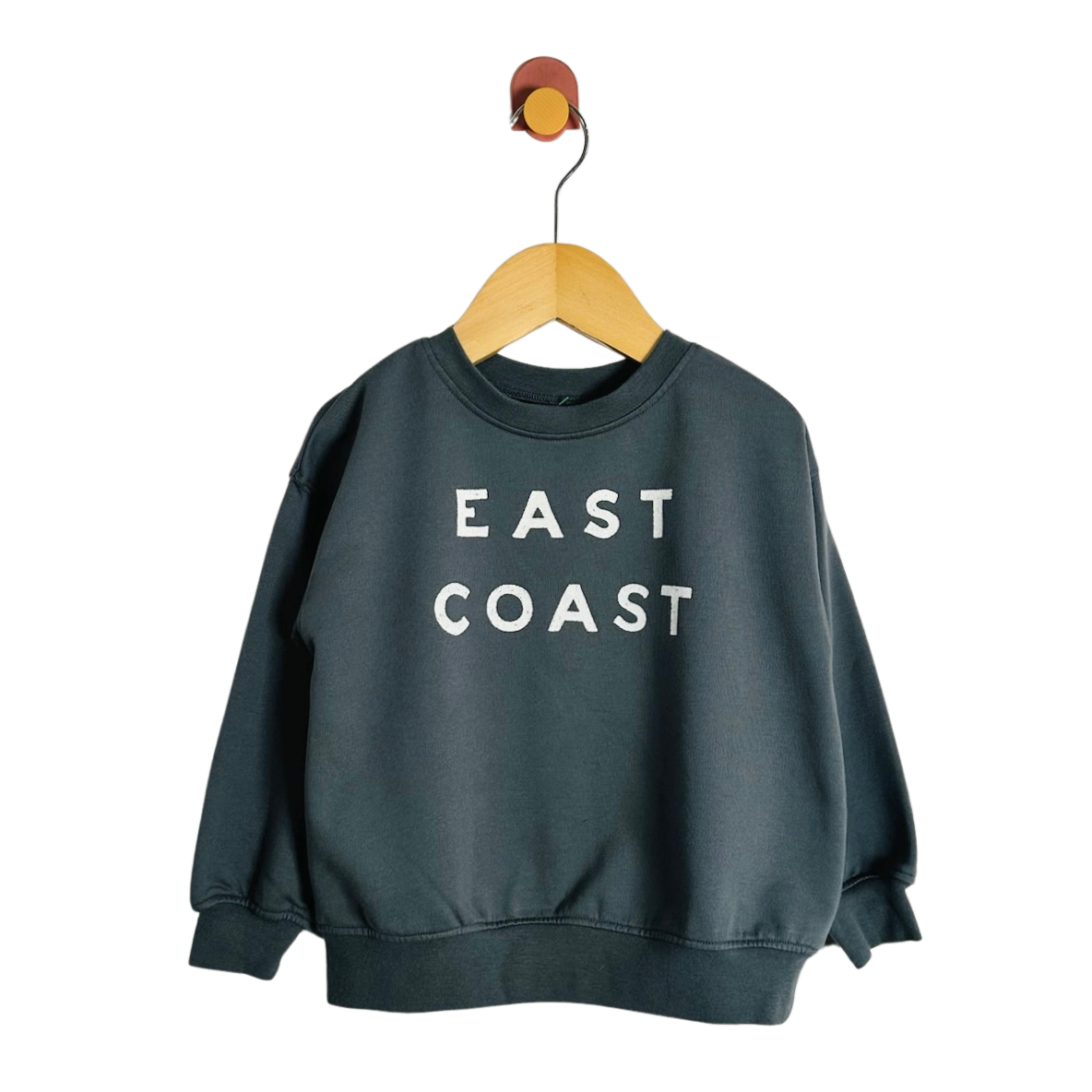 A dark slate green crewneck sweatshirt with 'EAST COAST' printed in white block letters on the chest, hanging on a wooden hanger against a plain white background.