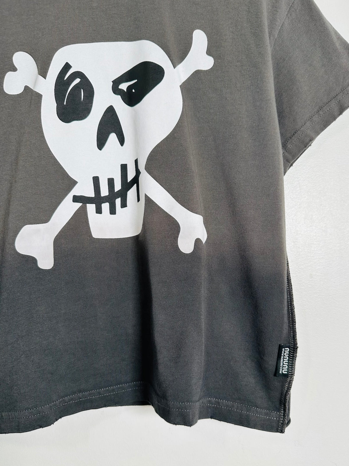 A close-up of a dark gray t-shirt featuring a large white skull and crossbones graphic with black details on the front.
