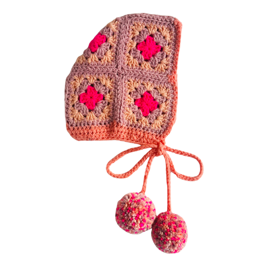 Crocheted baby bonnet with colorful squares and pom-poms on a white background